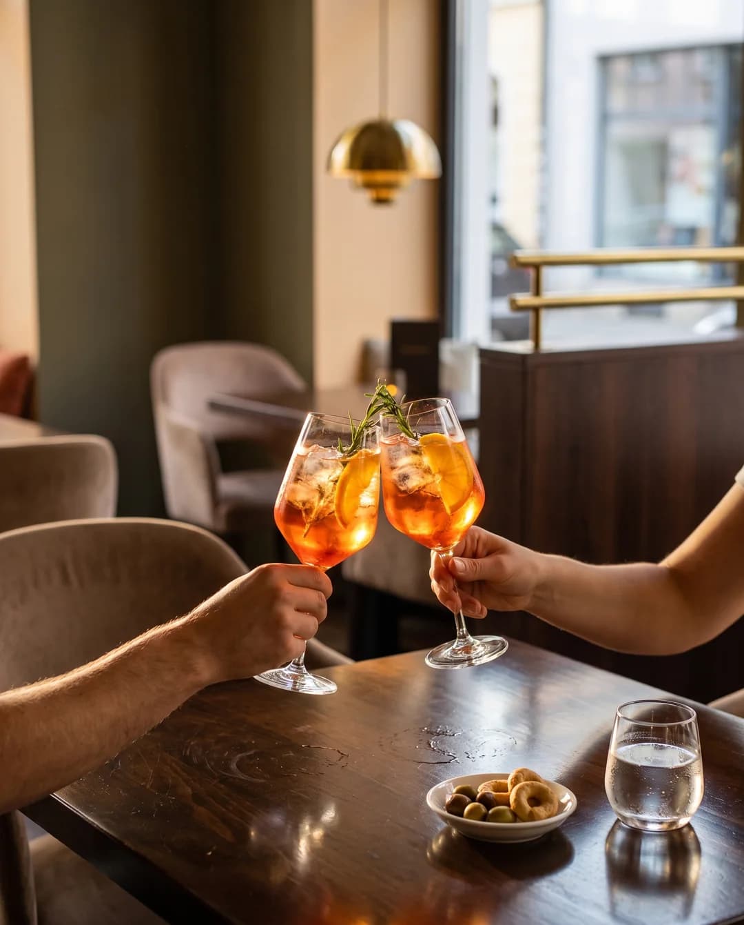 La-Commedia-Motiv mit zwei Aperitifgläsern in einer hellen Bar